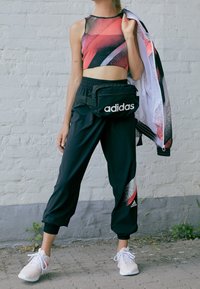 Black athletic pants with a tapered leg and elastic cuffs. Paired with a sleeveless red and black crop top and white sneakers. Black fanny pack.