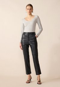 Grau langärmliges Oberteil kombiniert mit hochgeschnittenen schwarzen Lederhosen mit geradem Schnitt und sichtbaren Vordernähten; Model trägt schwarze Riemchenabsätze.