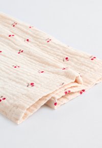 Tissu en coton beige doux avec un motif texturé et froissé, agrémenté de petites illustrations de cerises en rouge et rose, plié soigneusement.