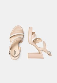 Sandali con tacco beige con design a tracolla incrociata e chiusura con fibbia. Parte superiore in pelle liscia con tacco a blocco e suola di colore chiaro.