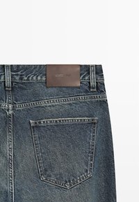 Jeans in denim blu scuro con un’etichetta in pelle marrone alla vita e una singola tasca posteriore contornata da cuciture in contrasto.