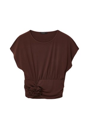 Blusa marrone a maniche corte con scollo rotondo, vita arricciata e fiore decorativo in tessuto sulla parte anteriore inferiore.