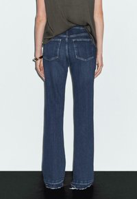 Ciemnoniebieskie spodnie dżinsowe o szerokich nogawkach i wysokim stanie, z dwoma tylnymi kieszeniami i surowym wykończeniem nogawek. Materiał wydaje się być dżinsowy z lekką teksturą.