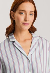 Lichtblauwe shirt met verticale rode en blauwe strepen. Heeft een kraag en een knoopsluiting aan de voorkant. Zijdezachte textuur.