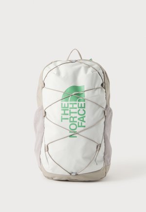 Mochila blanca y beige con el logo verde de "The North Face", cordón elástico frontal y bolsillos laterales de malla sobre un fondo liso.