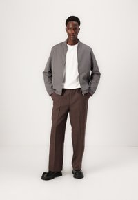 Gray bomber jacket with a zipper, white t-shirt underneath, and brown plaid trousers. Black chunky shoes complete the outfit.