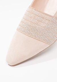 Chaussure beige à bout pointu avec un avant en daim et une bande tissée texturée comportant des fils métalliques. Finition lisse, silhouette élégante.