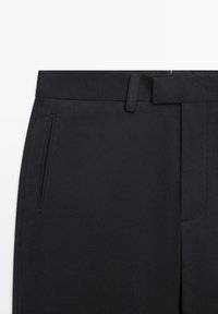 Pantaloni neri su misura con tasche laterali a fessura, passanti per cintura e chiusura frontale nascosta, mostrati dalla vita fino a metà coscia.