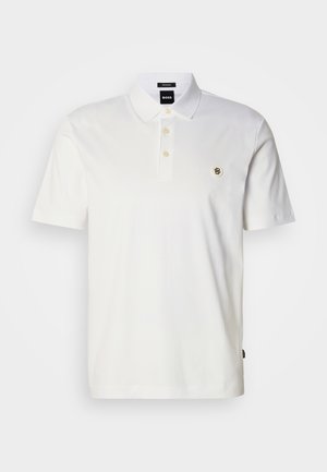 Valkoinen puuvillainen pikeepaita, jossa on kolmen napin lista, lyhyet hihat ja pieni kirjailtu logo vasemmassa rinnassa.