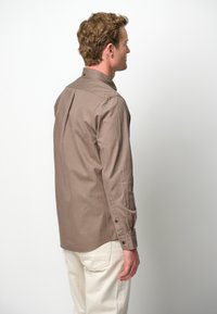 Bruine lange mouwen shirt met een knoopsluiting kraag, rechte snit en schouderplooien, gecombineerd met lichtgekleurde broeken. Glad textuur van de stof.