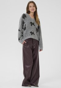 Maglione grigio a V con motivo di farfalla nera; abbinato a pantaloni larghi in ecopelle borgogna; texture liscia, vestibilità rilassata.