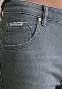 Grijze denim jeans met een aansluitend ontwerp, voorzien van een voorkeurszak en een merklabel. Kenmerkende stiksels langs de taille en de rand van de zak.
