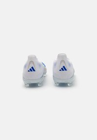 Scarpe da calcio bianche con accenti blu, materiale testurizzato, forma aerodinamica e tacchetti trasparenti su uno sfondo grigio chiaro e liscio.