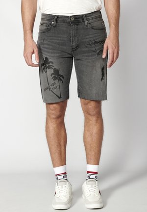 Pantalones cortos de mezclilla negra descolorida para hombre con estampado de palmeras y texto "Summer Vibes", combinados con calcetines blancos y zapatillas blancas.