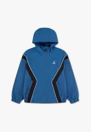 Blå hættetrøje med sorte og hvide chevron-striber på ærmer og front, lynlåslukning og et hvidt Jumpman-logo på brystet.