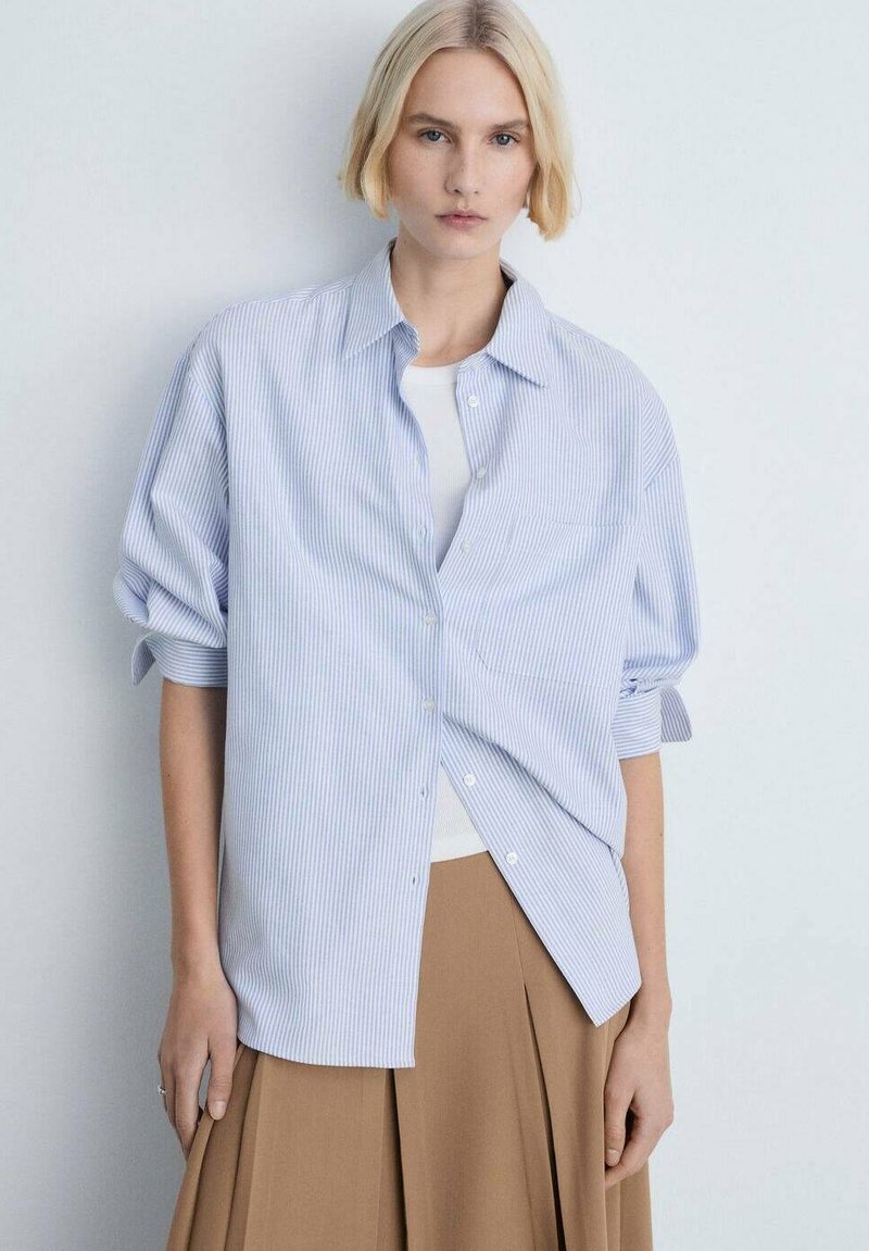 Light blue and white striped button-up shirt with rolled sleeves, featuring a relaxed fit and a smooth fabric texture. Notable mid-length cut.