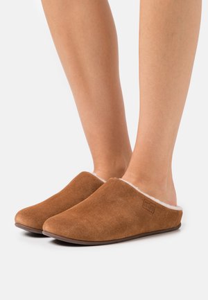Bruna mockaskor med en slip-on-design, utrustade med en fluffig vit foder och en rund tå. Läderlogotypdetalj på sidan.