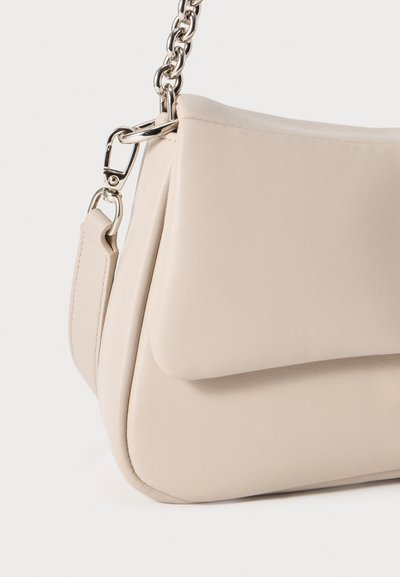 Μπεζ δερμάτινη τσάντα χειρός με λεία υφή, κλείσιμο με καπάκι και λουρί αλυσίδας σε ασημί χρώμα. Διαθέτει διακριτικό κυρτό σχήμα και μινιμαλιστικό σχεδιασμό.