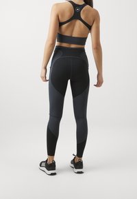 Completo sportivo nero composto da un reggiseno sportivo aderente e leggings a vita alta con diverse sfumature di grigio scuro, texture liscia e design elegante.