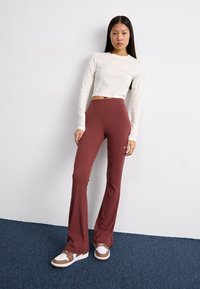 Leggings évasés couleur bordeaux en tissu extensible, associés à un haut court à manches longues couleur crème. Les baskets présentent des accents blancs et marron.