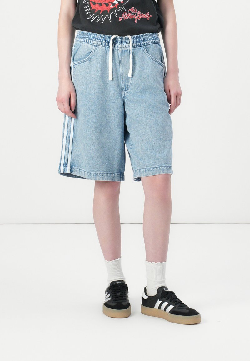 Shorts in denim di colore azzurro chiaro, lunghezza a metà coscia, con un elastico in vita e un cordino bianco. Presentano strisce bianche sui lati e tasche frontali.