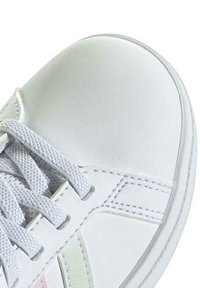 Sneaker bianco in pelle con punta arrotondata, lacci grigio chiaro e sottili strisce pastello sul lato. Texture liscia, design minimale.