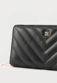 Czarny skórzany portfel z wzorem w jodełkę, złotym logo "HUGO" i zamknięciem na zamek błyskawiczny. Gładka faktura z estetycznym przeszyciem.