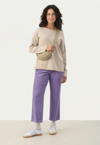 Béžový oversized svetr, fialové kordové kalhoty, bílé tenisky a crossbody taška, na jednobarevném pozadí s jemnými texturami.