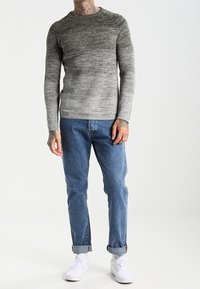 Grauer Ombre-Strickpullover mit langen Ärmeln und Rundhalsausschnitt; kombiniert mit hellblauen Jeans mit aufgerolltem Saum und weißen Sneakern.