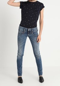 Marinblå t-shirt med vita prickar, kombinerad med blå skinny jeans. Jeanssen har en blekt textur och lätt slitage, kompletterat med svarta lägenheter.