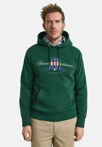 Donkergroene hoodie met een voorzak, voorzien van een bedrukte logo- en tekstontwerp in blauw, wit en rood. Geribde manchetten en zoom.
