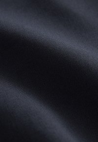 Gros plan d'un tissu bleu marine foncé montrant une texture fine, lisse et des plis subtils.