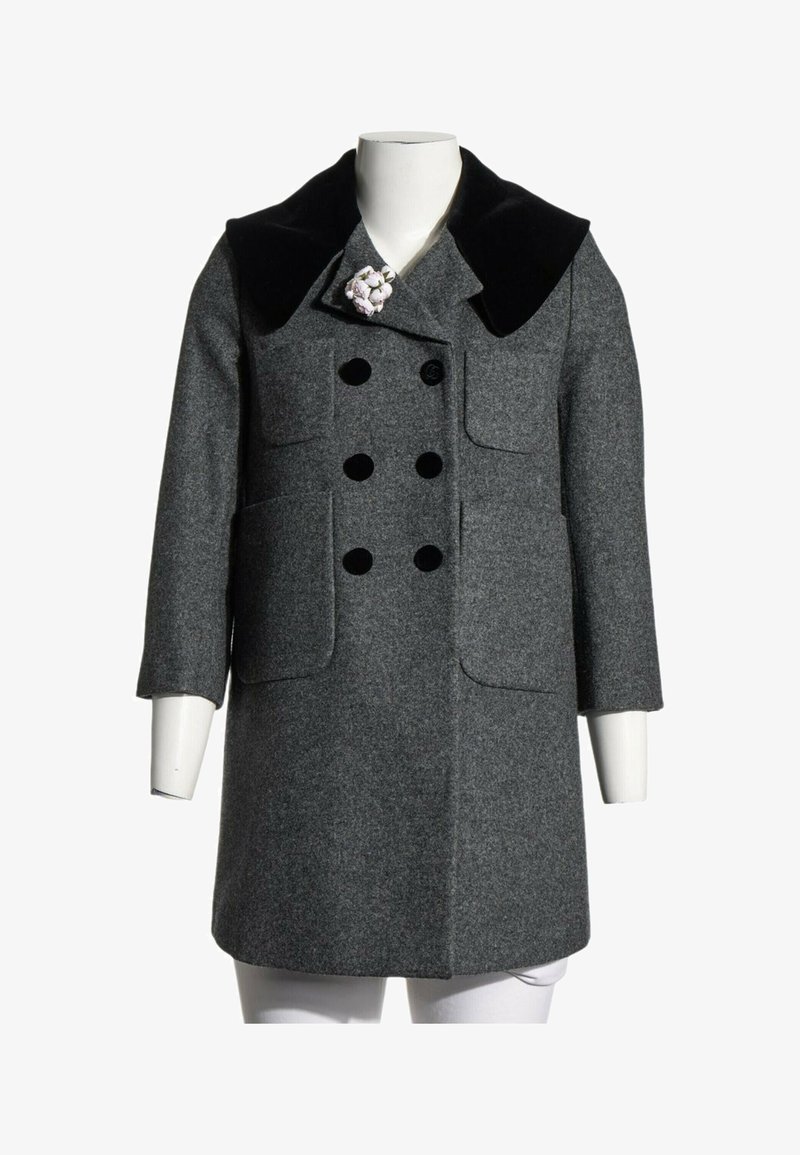 Manteau en laine gris à double boutonnage avec col en velours noir, deux poches avant et une épingle florale blanche sur le revers gauche, présenté sur un mannequin.