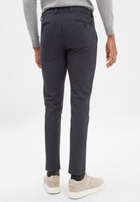 Slim-fit, ciemnoszare spodnie wykonane z teksturowanej tkaniny, z dwiema tylnymi kieszeniami zapinanymi na guziki. Połączone z jasnymi trampkami.