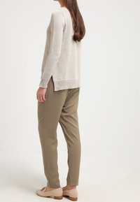 Hellebeige Strickpullover mit langen Ärmeln, seitlichen Schlitzen, kombiniert mit olivgrünen schmal geschnittenen Hosen und nudefarbenen flachen Schuhen mit einem kleinen Absatz.