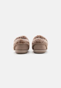Chaussons en daim marron avec un dessus doux et moelleux, forme arrondie, accents texturés et semelle blanche contrastante cousue.