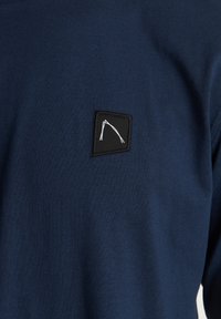 Marineblauer Pullover aus einem Baumwollmischgewebe, mit einem schwarzen quadratischen Patch und einem weißen geometrischen Liniendesign auf der Brust.