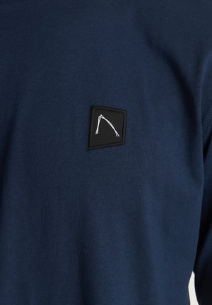 Námorně modrý svetr vyrobený z bavlněné směsi, s černým čtvercovým štítkem a bílým geometrickým vzorem na hrudi.