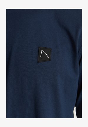Pullover blu navy realizzato in tessuto misto cotone, con una toppa quadrata nera e un design geometrico bianco sulla parte anteriore.