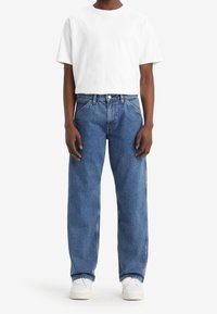 Witte t-shirt en blauwe loszittende denim jeans, met een klassiek vijf-pocket ontwerp en een rechte pijp. Witte sneakers maken de look af.