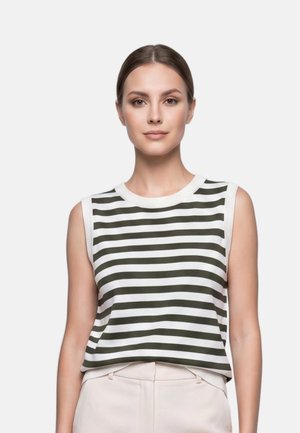 Jeune femme aux cheveux bruns attachés, portant un haut blanc sans manches avec des rayures noires horizontales et un pantalon clair.