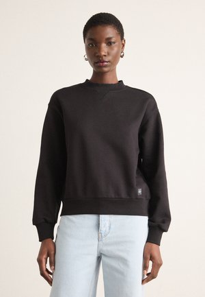 Svart crewneck genser med lange ermer, ribbede mansjetter og nederkant, laget av en blanding av bomull. Kombinert med lyseblå jeans.