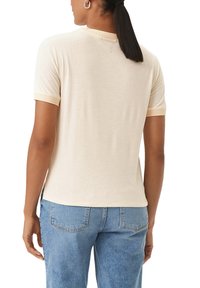 T-shirt beige a maniche corte con scollatura rotonda; presenta polsini a contrasto in crema e una texture morbida e liscia. Indossato con jeans azzurri chiari.