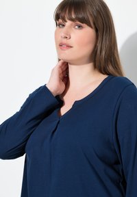 Camisa de manga larga azul marino con cuello redondo y un pequeño botón decorativo, hecha de una suave tela texturada.