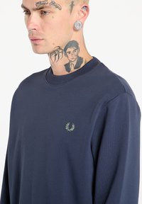 Felpa blu navy in cotone. Presenta un collo a giro e un logo ricamato sul petto. Texture liscia e vestibilità rilassata.