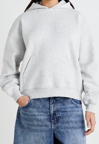 Ljusgrå hoodie med ficka framtill, avslappnad passform, ribbade mudd och fåll; mjuk textur, matchad med blå denimshorts.