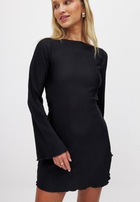 Vestido negro de manga larga con cuello barco, mangas acampanadas y dobladillo en forma de pico. Textura suave, diseño ajustado.