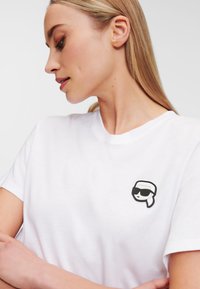 Witte katoenen T-shirt met een zwart-wit geborduurd ontwerp op de borst. Eenvoudige ronde hals en korte mouwen.