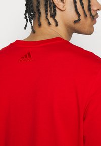 Sarkans kokvilnas t-krekls ar apaļu kakla izgriezumu un īsām piedurknēm. Adidas logo ir izšūts tumšāk sarkanā krāsā aizmugurē.