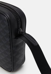 Pochette da viaggio nera realizzata in pelle liscia, caratterizzata da un motivo a logo in rilievo monocromatico, cerniera robusta e una tracolla in tessuto testurizzato.